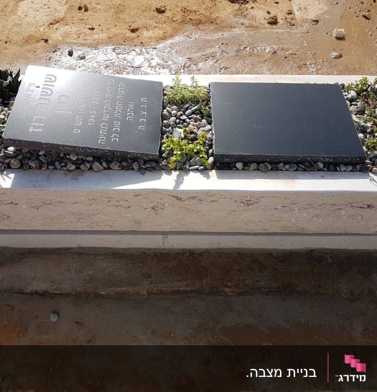 מצבה עם לוח אבן כהה ואבנים קטנות מסביב